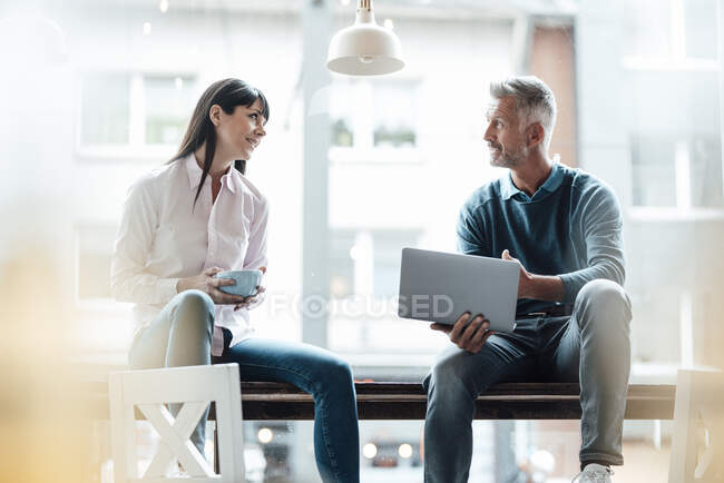 Male entrepreneur holding laptop while having discussion with female colleague at cafe — Stock Photo