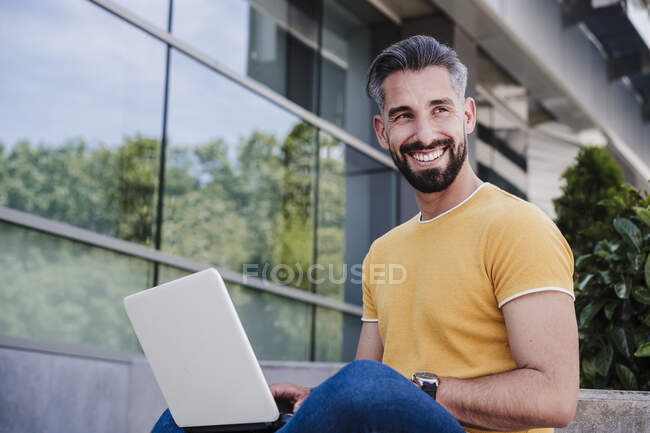 Lächelnder Geschäftsmann mit Laptop, der wegschaut — Stockfoto