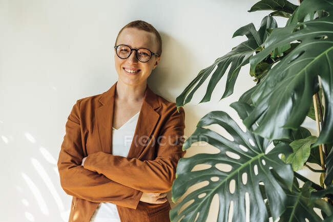 Imprenditrice sorridente con le braccia incrociate dalla pianta — Foto stock