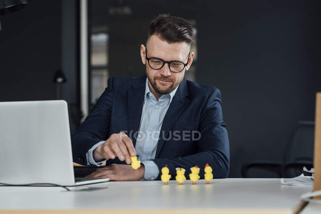 Empresario masculino con computadora portátil sosteniendo juguete de pollo bebé en la oficina - foto de stock