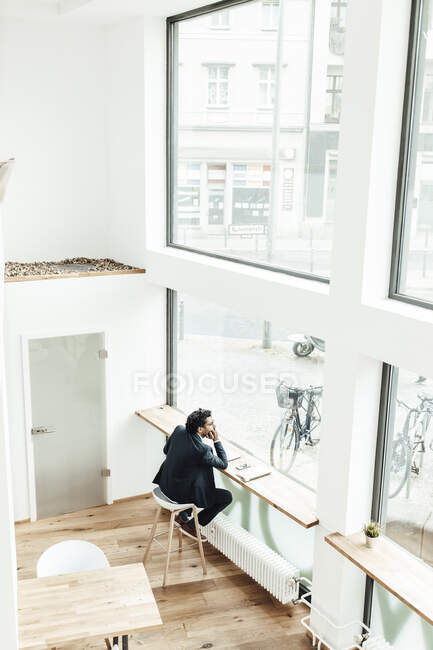 Nachdenklicher reifer Geschäftsmann sitzt am Schreibtisch und schaut durchs Bürofenster — Stockfoto