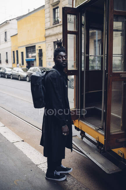 El hombre a la moda con la mochila de pie junto al tranvía en el sendero - foto de stock