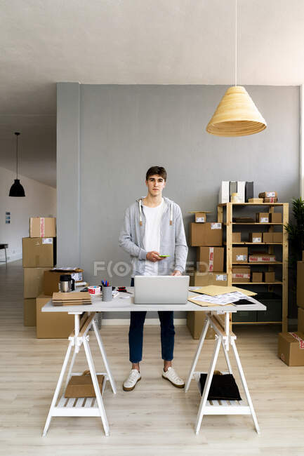 Empresário com telefone inteligente em pé na mesa no escritório — Fotografia de Stock