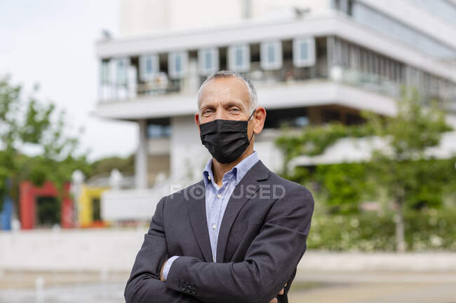 Uomo d'affari con maschera protettiva vicino edificio in città durante COVID-19 — Foto stock
