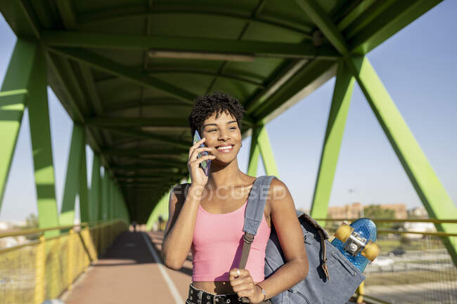 Посміхнена жінка з рюкзаком говорить на смарт-телефоні в бриджі. — стокове фото