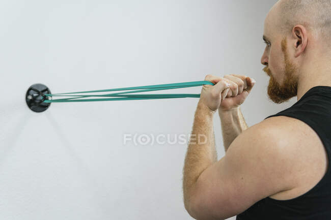Mann übt Bizeps-Übung durch Widerstandsband an Wand im Fitnessraum gefesselt — Stockfoto