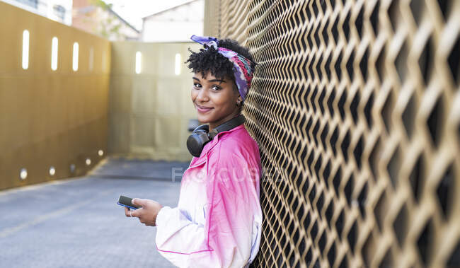 Чудова молода жінка з навушниками, що тримають мобільний телефон за стіною. — стокове фото