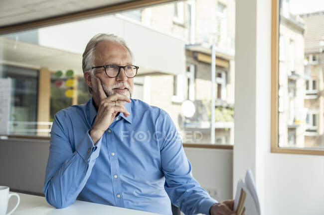 Maturo maschio professionista con documenti guardando altrove mentre seduto alla scrivania in ufficio — Foto stock