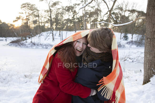 Весела молода пара насолоджується під час обгортання в ковдрі взимку — стокове фото