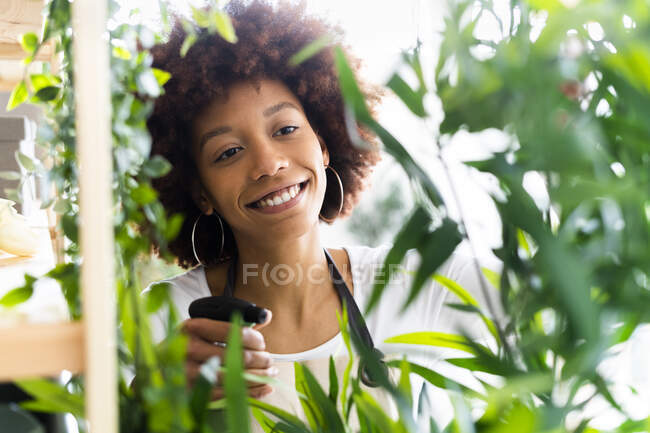 Lächelnde Floristin sprüht Wasser auf Pflanze im Geschäft — Stockfoto