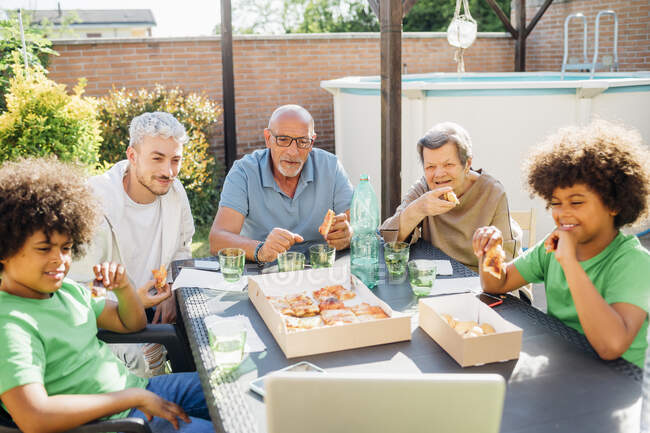 Famiglia multietnica mangiare cibo mentre seduti insieme in cortile — Foto stock