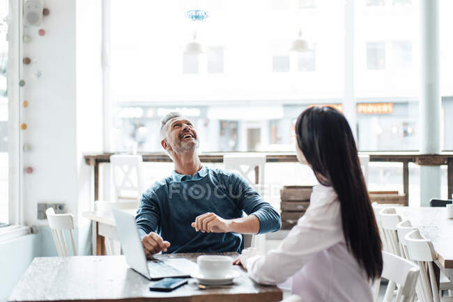 Hombre de negocios sonriente mirando al dron mientras está sentado con su colega en la cafetería - foto de stock