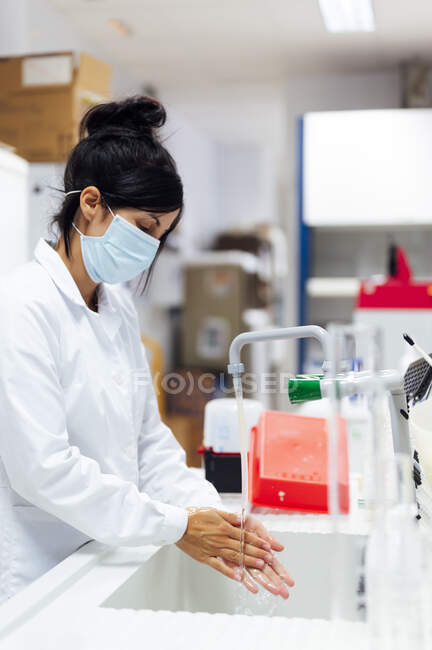 Chercheuse mature portant un masque protecteur pour le visage se laver les mains en laboratoire — Photo de stock