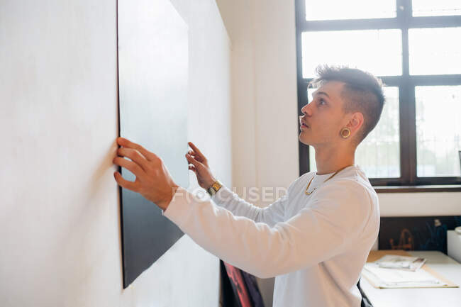 Giovane hipster uomo attaccare cartone nero sulla parete in studio — Foto stock