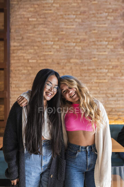 Sorridente amiche con il braccio intorno in piedi nel bar — Foto stock
