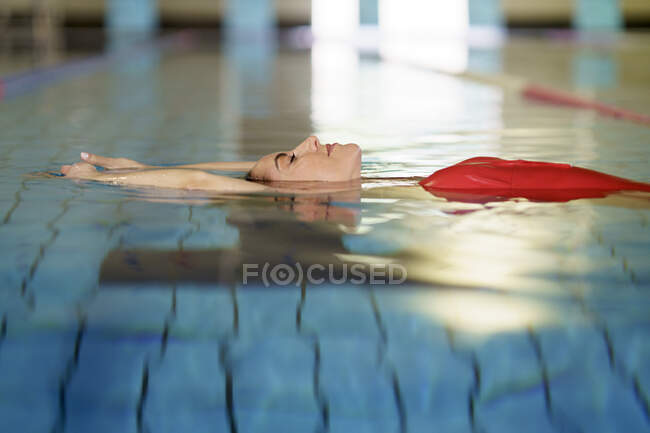 Donna con gli occhi chiusi galleggiante sull'acqua in piscina — Foto stock