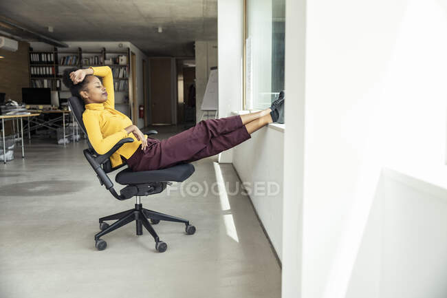 Безробітна жінка з ногами в офісі відпочиває на кріслі — стокове фото
