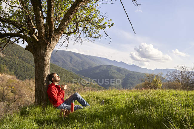 Mann in roter Jacke lehnt an Baum und genießt die Natur — Stockfoto