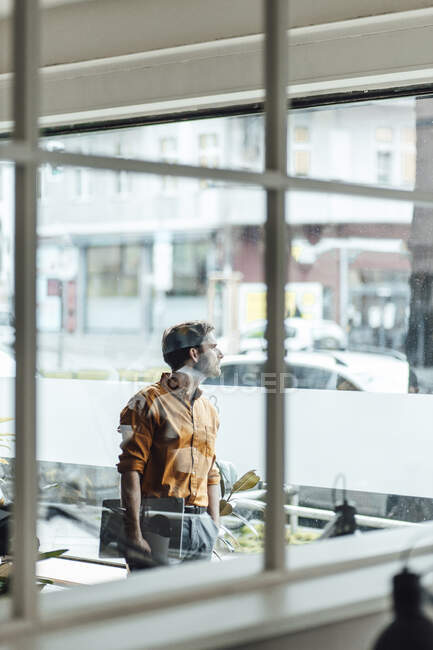 Male entrepreneur with digital tablet looking through window in office — Stock Photo