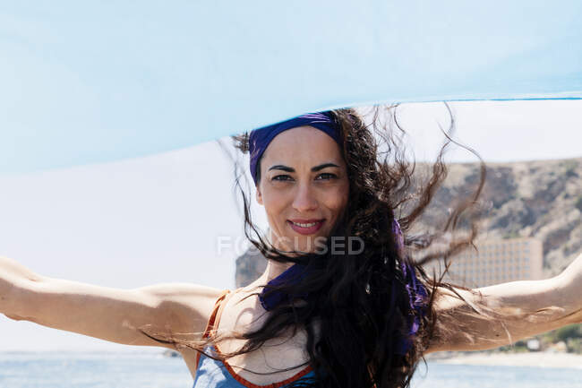 Bailarina sonriente sosteniendo sarong azul en día soleado - foto de stock