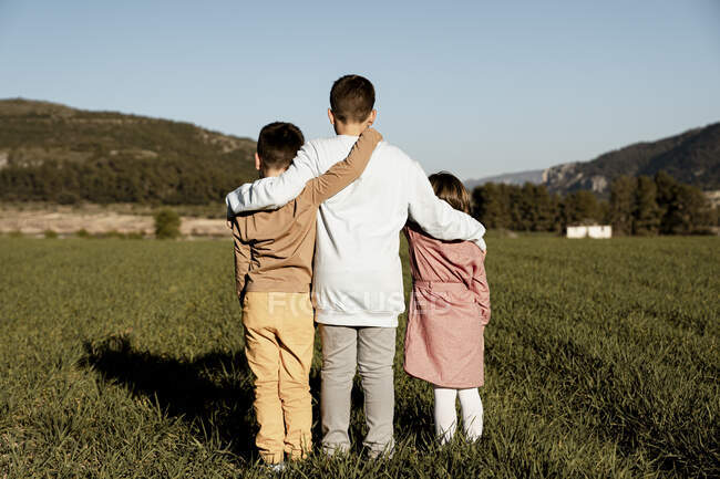 Fratelli e sorelle in piedi con le braccia intorno sul campo agricolo — Foto stock