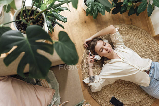 Frau mit erhobenen Händen hört Musik während sie es sich zu Hause auf Teppich gemütlich macht — Stockfoto