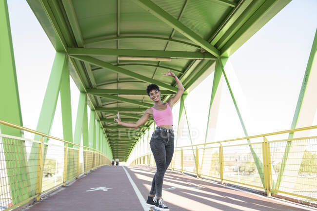 Усмішка молода жінка робить знак миру стоячи на мосту. — стокове фото