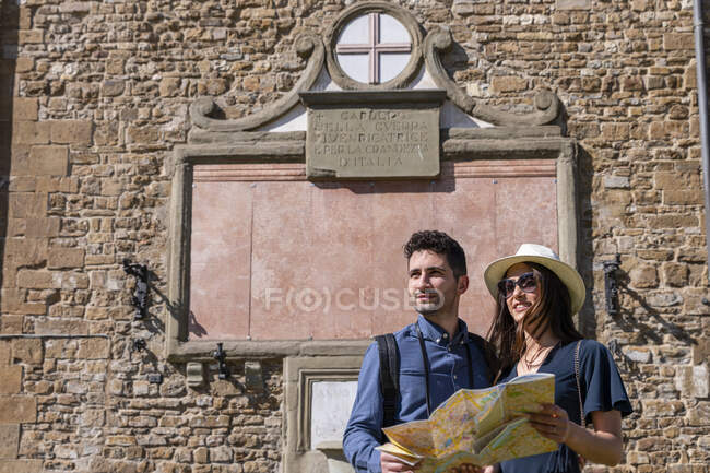 Туристическая пара держит карту перед кирпичной стеной — стоковое фото