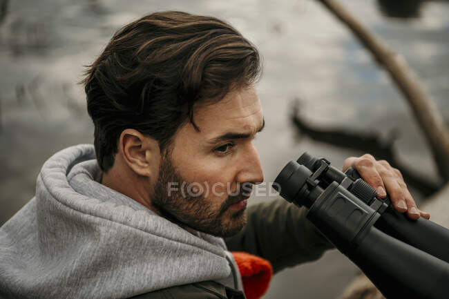 Hombre guapo con barba sosteniendo binoculares mientras mira hacia otro lado - foto de stock