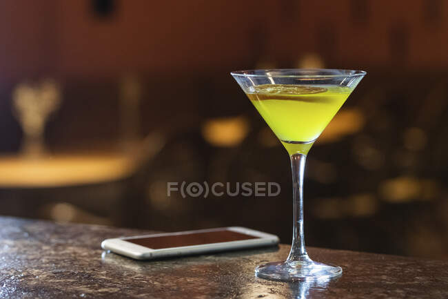 Напитки в бокале мартини по мобильному телефону на столе — стоковое фото