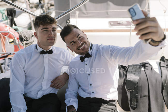 Uomo sorridente scattare selfie con amico maschio attraverso il telefono cellulare in yacht — Foto stock