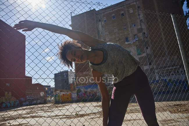 Sportswoman faire de l'exercice d'étirement devant la clôture de chaînette sur la journée ensoleillée — Photo de stock