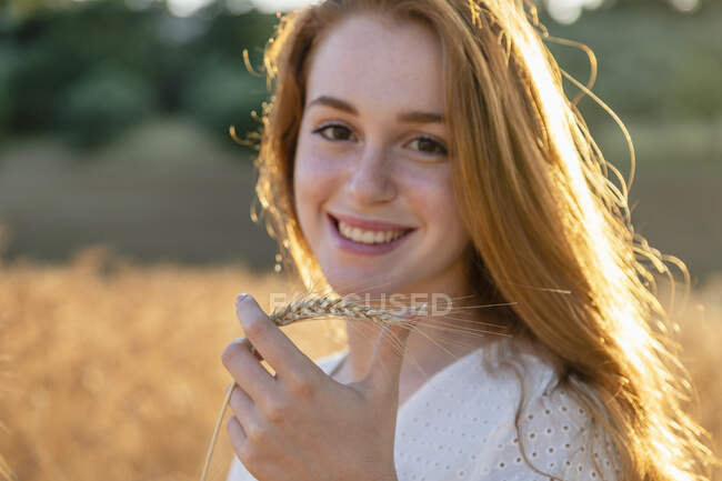 Hermosa mujer sosteniendo espiga de trigo sonriendo en día soleado - foto de stock