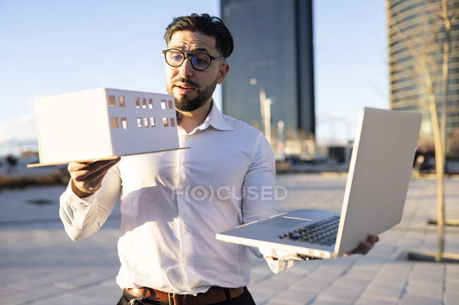 Architetto maschio mostra modello architettonico durante la videochiamata attraverso il computer portatile mentre in piedi sul sentiero — Foto stock