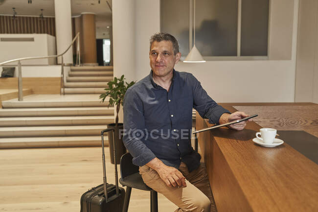 Зрілий бізнесмен тримає цифрову табличку, сидячи за столом. — стокове фото