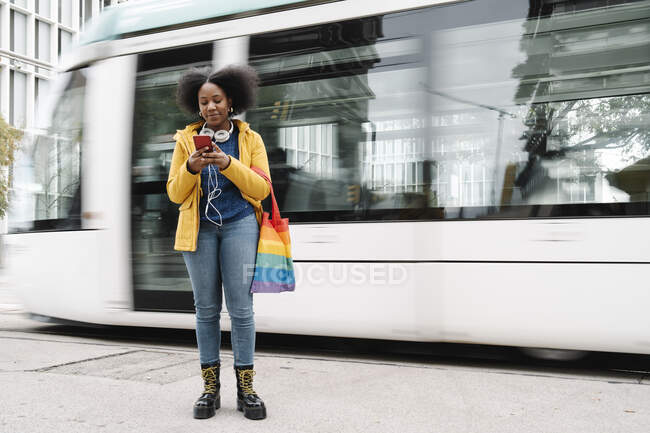 Молода жінка пише повідомлення по мобільному телефону, стоячи на дорозі проти трамвая. — стокове фото