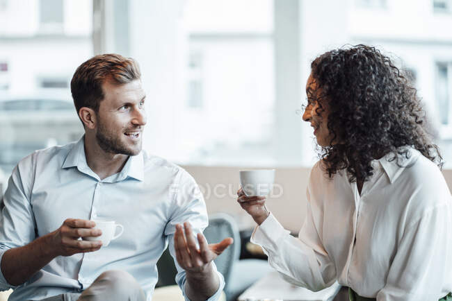 Sonriente gente de negocios hablando mientras toma café sentado en la cafetería - foto de stock