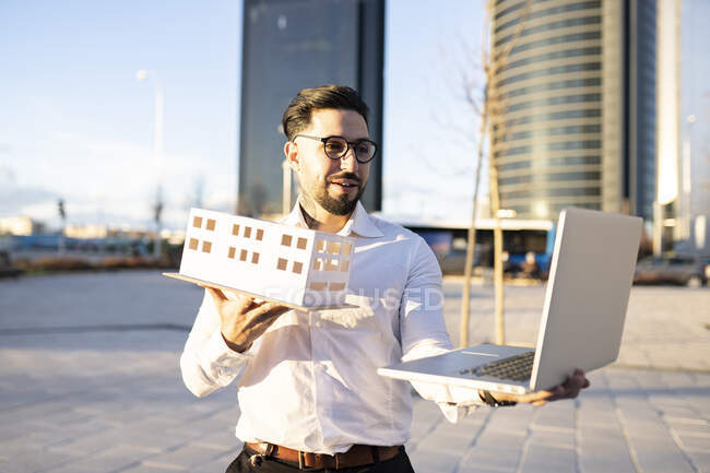 Архитектор-мужчина показывает архитектурную модель во время видеозвонка через ноутбук на тропинке — стоковое фото