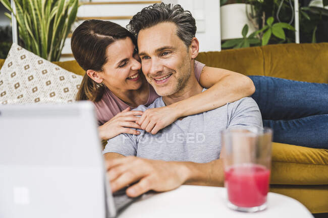 Donna sorridente che abbraccia l'uomo utilizzando tablet digitale a casa — Foto stock