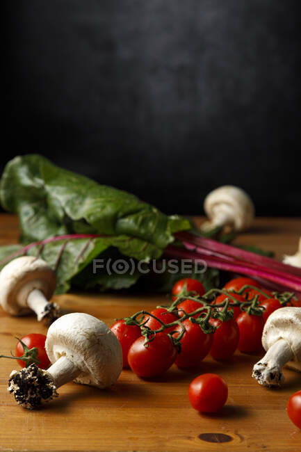 Ruby red chard with edible mushrooms and cherry tomatoes on wooden table — Stock Photo