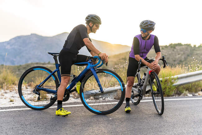 Des cyclistes souriants parlent assis sur des vélos pendant le coucher du soleil — Photo de stock
