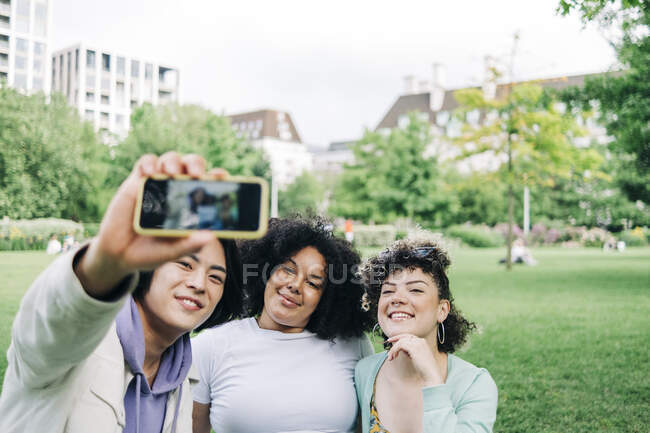 Sorridente maschio e femmina amici prendendo selfie al parco — Foto stock