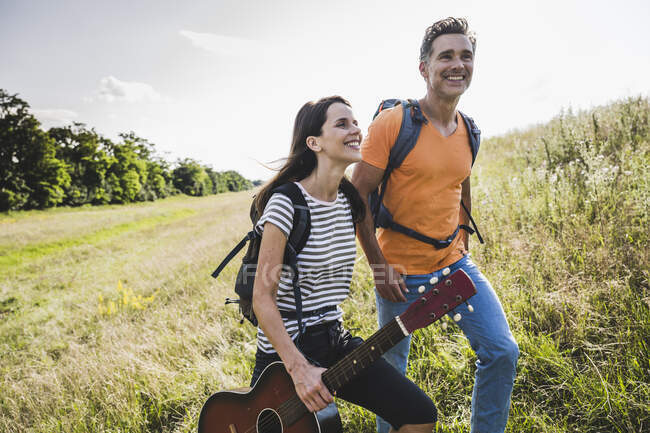 Woman holding guitar while hiking with man on grass — Stock Photo