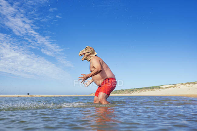 Hombre con máscara de lagarto haciendo gestos en el mar en la playa - foto de stock