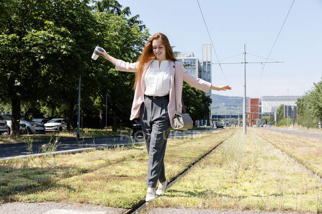 Businesswoman with arms outstretched balancing on railroad track during sunny day — Stock Photo