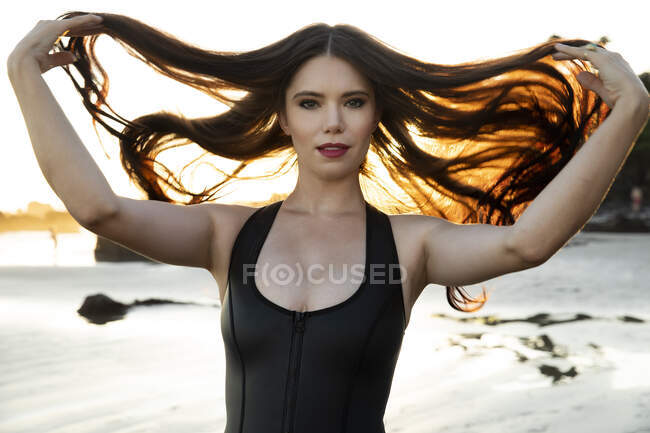 Modelo de moda jugando con el pelo negro largo en la playa - foto de stock