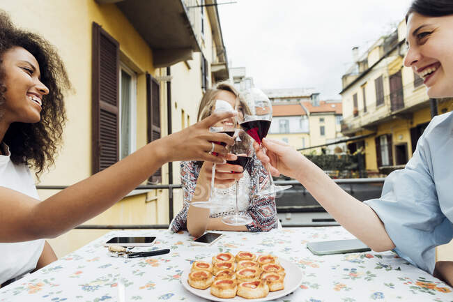 Lächelnde junge Freunde stoßen am Tisch mit einem Weinglas an — Stockfoto
