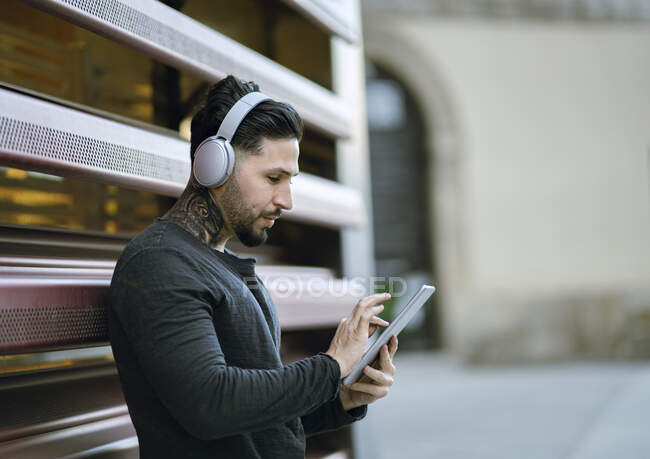 Hombre guapo con auriculares usando tableta digital contra pared de metal - foto de stock