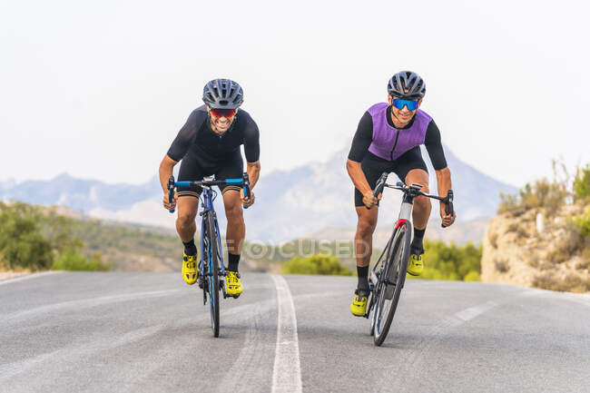 Smiling male cyclists riding bicycles together on road — Stock Photo