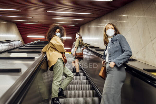Friends with protective face mask standing at social distance on escalator — Stock Photo